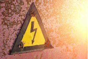 Old, rusty warning about danger and high voltage in form lightning yellow background. photo