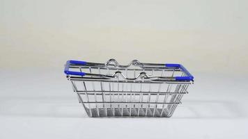 Metal decorative small shopping basket with blue handles rotates on a white background. Many different pills fall from above. Being filled with tablets. video