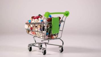 pequeño carrito de compras decorativo de metal con asas verdes gira sobre un fondo blanco. lleno de tabletas. un montón de pastillas en el carrito. video