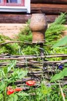 wattle hurdle with old clay pot and log house photo