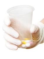 gloved hand holding plastic cup with pills photo