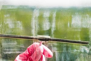 hand in pink glove cleans window glass by squeegee photo