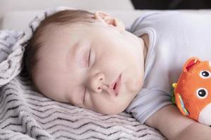 niño adorable, con un juguete favorito, duerme relajado y se recuesta en la cama de los padres foto