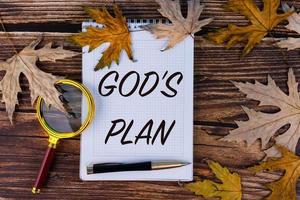 God's plan, the text is written in a white notebook with a pen on a background of autumn, maple leaves and old boards. photo