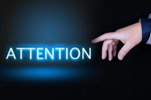 ATTENTION text, word written in neon letters on a black background pointed to by a hand with a person's index finger. photo