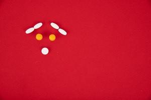 The pills are stacked in the form of a sad smiley on a red background. Copyspace photo