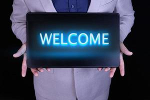 WELCOME text, word written in neon letters on a black laptop, in front of a businessman in a gray suit. photo