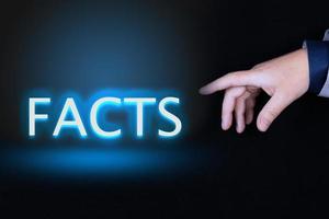 FACTS text is a word written in neon letters on a black background pointed to by a hand with a person's index finger. photo