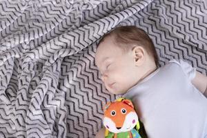 Adorable child, with a favorite toy, sleeps relaxed and sprawls on the parents' bed photo