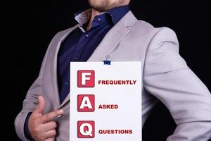 A businessman holds a blank sheet of paper with the text abbreviated as FAQ Frequently Asked Questions. Business concept. photo