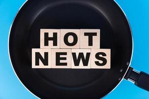 HOT NEWS word, text written on wooden cubes, building blocks lying on a frying pan and a blue background.