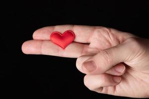 A woman's hand, palm, gesture, makes a gun with her fingers, on which lies a red heart. photo