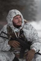 guerra de invierno en las montañas árticas. operación en condiciones frías. soldado en uniforme camuflado de invierno en el ejército de guerra moderno en un día de nieve en el campo de batalla del bosque con un rifle. enfoque selectivo foto