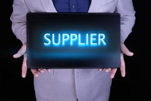 SUPPLIER word, text written in neon letters on a laptop which is being held by a businessman in a gray suit. photo