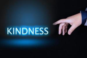 KINDNESS text, word written in neon letters on a black background pointed to by a hand with a person's index finger. photo