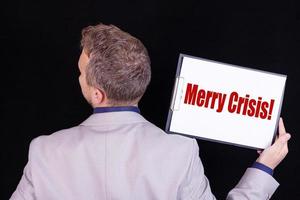 A businessman holds a blank sheet of paper with the text MERRY CRISIS. Business concept. photo