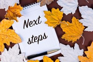 Next Steps, inscription, text, in a white notebook on a background of autumn, maple leaves. photo