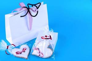 Valentine's Day cookies. Sweet heart-shaped cookies and white paper bag. Homemade baking. View from above. Blue background. Copy space. photo
