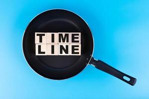 TIMELINE word, text written on wooden cubes, building blocks lying on a frying pan and a blue background. photo