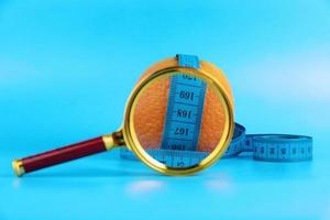 Diet concept with measuring tape, orange and magnifying glass for weight loss on blue background. photo