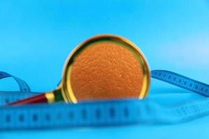 Magnifying glass and orange on a blue background as a symbol of cellulite. Concept Anti-cellulite program. photo