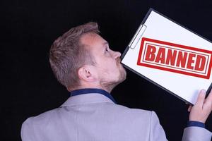 A businessman holds a blank sheet of paper with the text Banned. Business concept. photo