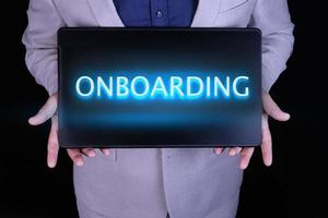 ONBOARDING word, text written in neon letters on a laptop which is being held by a businessman in a gray suit. photo