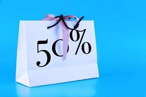 White paper bag, shopping bag with 50 percent sign on blue background. Copy space. photo