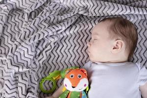 Adorable child, with a favorite toy, sleeps relaxed and sprawls on the parents' bed photo