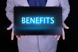 BENEFITS text, word written in neon letters on a black laptop, in front of a businessman in a gray suit. photo