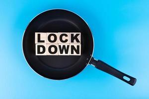 LOCKDOWN word, text written on wooden cubes, building blocks lying in a frying pan, and blue background. photo