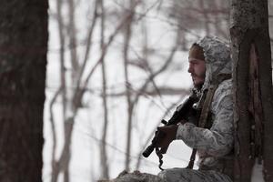 Winter war in the Arctic mountains. Operation in cold conditions.Soldier in winter camouflaged uniform in Modern warfare army on a snow day on forest battlefield with a rifle. Selective focus photo