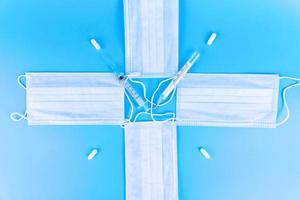 Disposable blue medical masks are folded in the form of a clock, in the form of a cross with a thermometer, a syringe and pills. photo