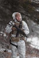 guerra de invierno en las montañas árticas. operación en condiciones frías. soldado en uniforme camuflado de invierno en el ejército de guerra moderno en un día de nieve en el campo de batalla del bosque con un rifle. enfoque selectivo foto