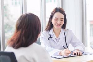 Asian professional doctor woman who wears medical coat talks with female patient to suggest treatment guideline and healthcare concept in office of hospital. photo