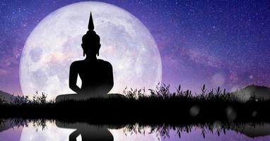 Silhouette of Buddha mediating with Full moon at night. Buddhist holiday Concept. photo
