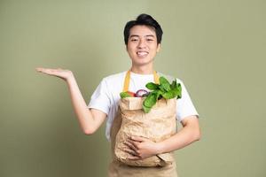 Young man is holding a bag full of vegetables, on white background. photo