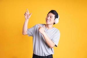 image of asian man listening to music with headphones, isolated on yellow background photo