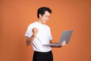 asian man holding laptop, isolated on orange background photo