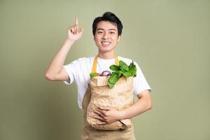 Young man is holding a bag full of vegetables, on white background. photo