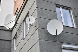 Satellite dish on a gray building close-up. A parabolic antenna on the wall. photo