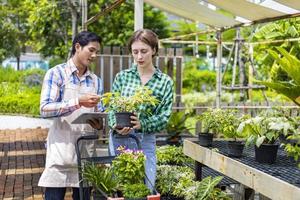 Young caucasian customer is asking the nursery owner about the exotic plant with shopping cart full of summer plant for weekend gardening and outdoor pursuit photo