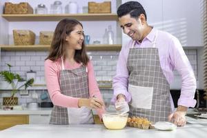 una pareja de diferente diversidad se ayuda mutuamente en la preparación de comidas mezclando harina para hornear pan en una cocina blanca y moderna foto