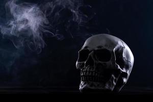 cráneo humano de halloween en una vieja mesa de madera sobre fondo negro. forma de hueso del cráneo para la cabeza de la muerte en el festival de halloween que muestra horror, miedo al diente malvado y miedo con humo de niebla, espacio de copia foto