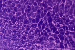 Defocus blurred transparent purple colored clear calm water surface texture with splash, bubble. Shining purple water ripple background. Surface of water in swimming pool. Tropical purple water color. photo