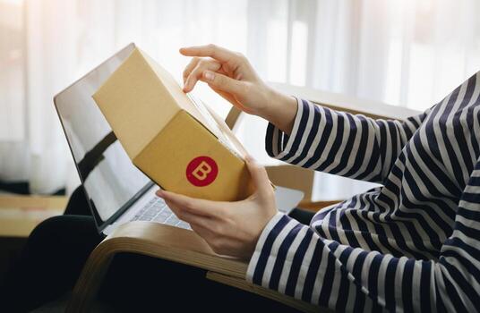 Online merchandising business idea, beautiful girl holding a parcel delivery box and using a computer to input Track And Trace parcel numbers to customers. photo
