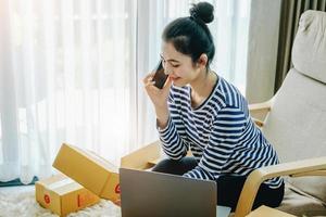 Online merchandising business idea, beautiful girl talking on the phone and holding a parcel box ready to use a computer to enter the Track And Trace parcel number to the customer. photo