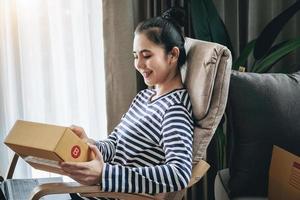 Online merchandising business idea, beautiful girl holding a parcel delivery box and using a computer to input Track And Trace parcel numbers to customers. photo