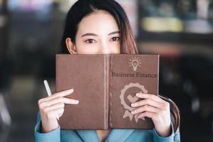 empresaria asiática o mujer de negocios que muestra una cara sonriente mientras lee un libro que desarrolla estrategias financieras y de inversión. foto