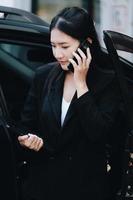 Asian businessmen, business owners, company presidents or female employees talking on the phone and holding a tablet are getting out of the car to attend a business plan meeting at the meeting. photo